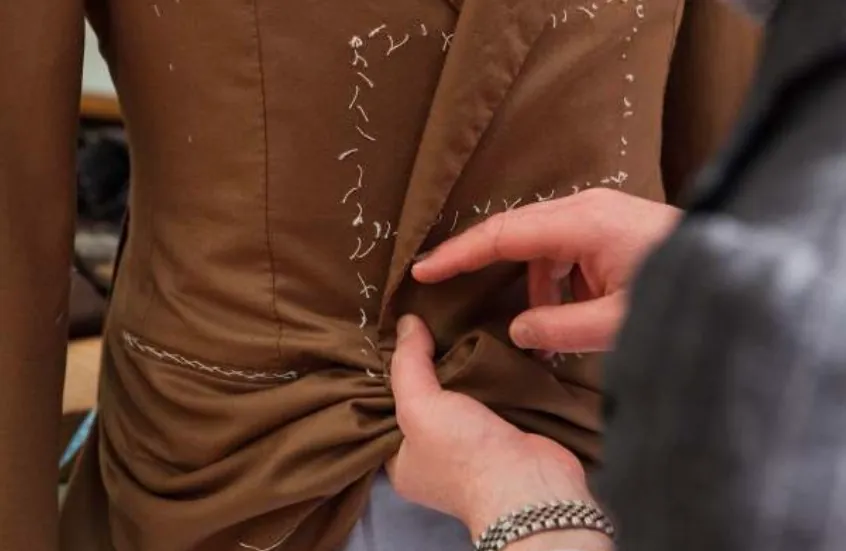 A tailor adjusting the waist of a brown jacket